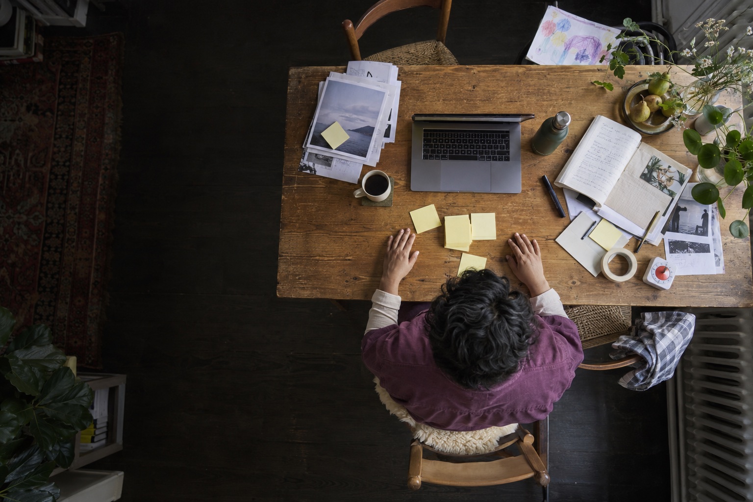 Directly overhead view of a facilitator in a plum overshirt arranging yellow notes and workshop materials at home.